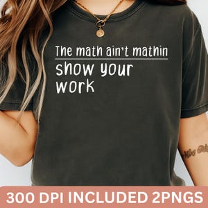 Puede incluir: Camiseta gris oscuro con el texto blanco "The math ain't mathin show your work". La camiseta tiene cuello redondo y mangas cortas. La parte inferior de la imagen tiene el texto "300 DPI INCLUDED 2PNGS" en una pancarta rosa.