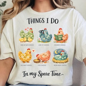 Könnte beinhalten: Cremefarbenes T-Shirt mit dem Text "THINGS I DO" über illustrierten Hühnern. Das Shirt zeigt verschiedene Aktivitäten zum Thema Hühner, wie "Hang out with Chickens" und "Dream about Chickens". Der Satz "In my Spare Time" steht darunter.