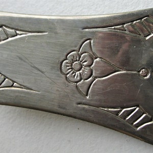 May include: A silver cake server with an ornate design featuring a stylized flower and geometric patterns.