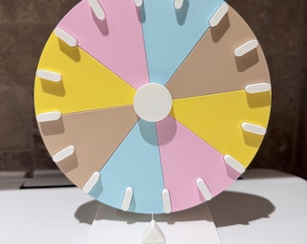 May include: A colorful, segmented wheel with pastel sections of pink, blue, yellow, and tan. White, rectangular markers are evenly spaced around the wheel's perimeter. The wheel is mounted on a white, rectangular base.