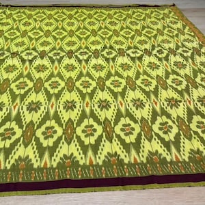 Peut inclure: Un textile rectangulaire présentant un motif répétitif de losanges vert citron et vert olive contenant des motifs floraux. Le tissu comprend de fines rayures verticales orange et une bordure unie violet foncé sur le bord inférieur.