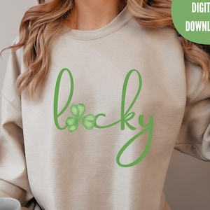 May include: A beige sweatshirt with the word "Lucky" in green script, and a shamrock. The upper right corner has a green circle with the words "DIGITAL DOWNLOAD" in white. The sweatshirt is a casual style.