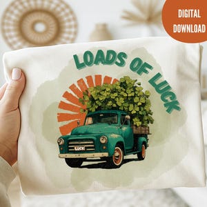 Könnte beinhalten: Ein cremefarbenes T-Shirt mit einem vintage tealfarbenen Truck, der mit Kleeblättern beladen ist. Der Text "LOADS OF LUCK" ist über dem Truck aufgedruckt, mit einem orangefarbenen Sonnenstrahlendesign im Hintergrund. Die Worte "DIGITAL DOWNLOAD" stehen in einem Kreis.