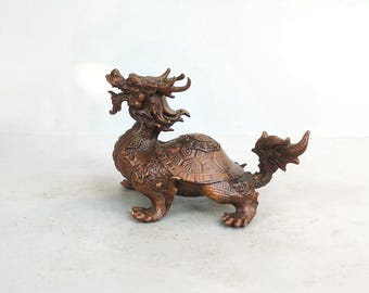 May include: A bronze-colored statue of a mythical creature, a hybrid of a dragon and a turtle. The statue has intricate details, including scales, horns, and a detailed shell. The creature is in a standing position, with its head raised and its tail curled.