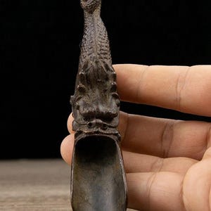 Peut inclure: Une cuillère de couleur bronze avec un motif de dragon. La cuillère présente une tête de dragon détaillée en haut et une cuillère en forme de bol en bas. Les écailles et les traits du dragon sont finement sculptés, créant une pièce décorative unique.