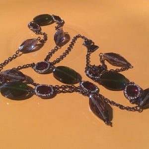 May include: A black chain necklace with green and brown oval-shaped beads and small red gemstone accents.