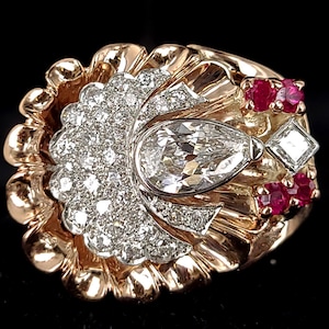 May include: A gold ring with a large pear-shaped diamond surrounded by smaller diamonds and red rubies. The ring has a textured, scalloped design.