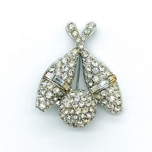 May include: A silver tone brooch featuring a bowling pin design. The pins are set with clear rhinestones and have a gold tone accent. The ball is also set with clear rhinestones.