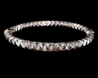 May include: A silver bangle bracelet with a woven chevron pattern.