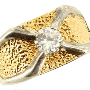 Puede incluir: Un anillo de oro y plata con una gran piedra preciosa redonda y transparente en el centro. El anillo tiene un diseño texturizado.