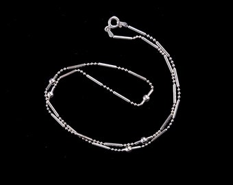May include: A silver chain necklace with a delicate design featuring alternating round and bar-shaped links. The necklace has a simple clasp closure.