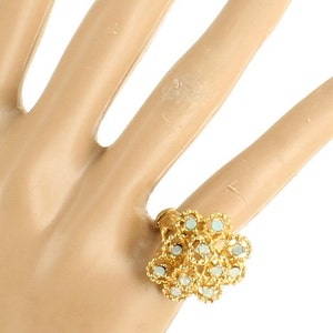 May include: A gold ring with a flower design featuring white stones. The ring is on a model's finger.