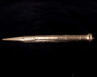 May include: A gold-toned mechanical pencil with a detailed engraved design. The pencil has a pointed tip and a cap on the end.