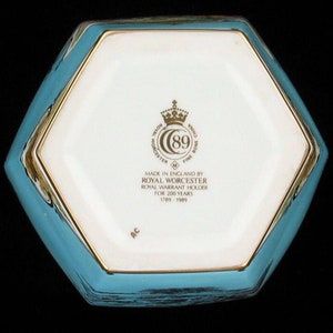 May include: The bottom of a hexagonal porcelain box with a blue and gold design. The box has a Royal Worcester logo with the text "Made in England by Royal Worcester, Royal Warrant Holder for 200 Years, 1789-1989".