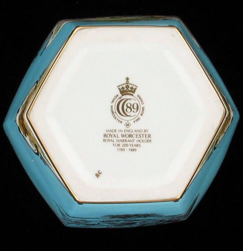 May include: The bottom of a hexagonal porcelain box with a blue and gold design. The box has a Royal Worcester logo with the text "Made in England by Royal Worcester, Royal Warrant Holder for 200 Years, 1789-1989".