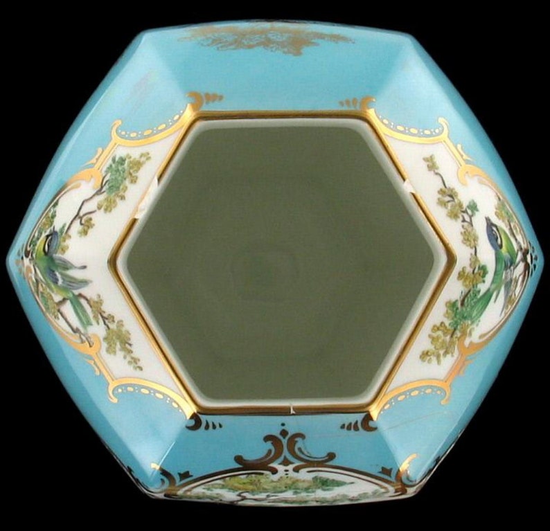May include: A hexagonal porcelain bowl with a light blue glaze and gold trim. The bowl features a floral design with birds and green leaves. The inside of the bowl is white.