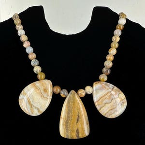 May include: A necklace made of brown, white, and beige agate beads with three large teardrop-shaped agate pendants.