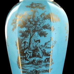 May include: A blue and gold porcelain vase with a lid. The vase is decorated with a pastoral scene of two figures and sheep in a landscape. The lid is decorated with a bird.