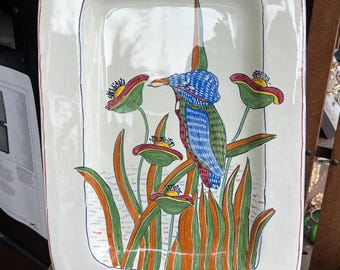 May include: Rectangular white ceramic serving platter with a hand-painted design. The design features a colorful bird with blue, green, and red details, surrounded by stylized flowers and foliage in orange, green, and red. The platter has a red and blue border.