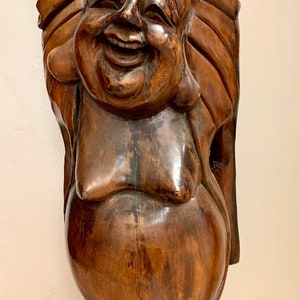 May include: A large, wooden sculpture of a laughing Buddha with raised arms. The sculpture is carved from dark brown wood and has a detailed face with a wide smile.