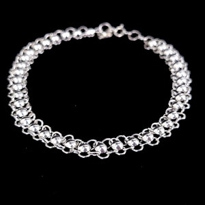 May include: A silver chain bracelet with a delicate design. The bracelet is made of small, round links that are connected together to form a continuous chain.