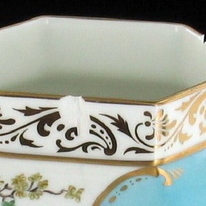 May include: A white porcelain octagonal sugar bowl with a gold rim and a blue and gold floral design. The bowl has a white interior.