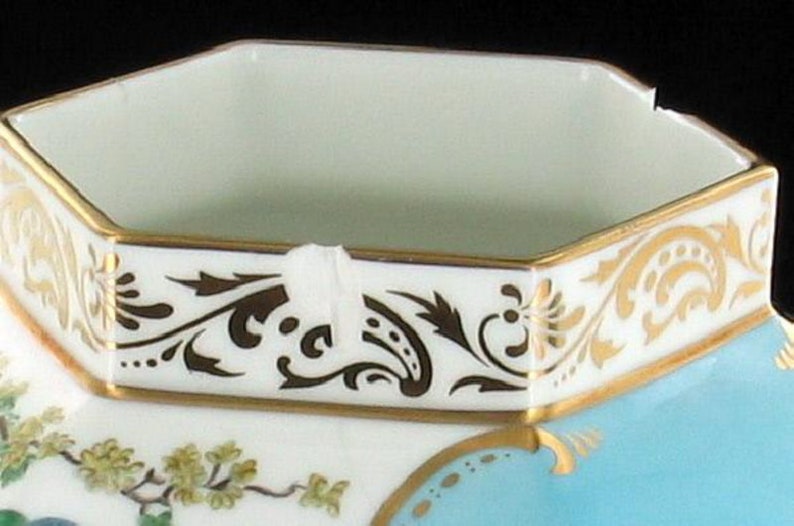 May include: A white porcelain octagonal sugar bowl with a gold rim and a blue and gold floral design. The bowl has a white interior.