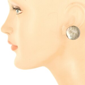 May include: A pair of round, silver-toned earrings with a mother-of-pearl inlay. The earrings are a light gray color with a subtle shimmer.