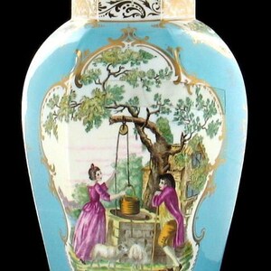 May include: A blue and white porcelain vase with a gold trim and a painted scene of a couple by a well. The lid of the vase has a gold finial and a painted bird.