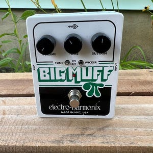 May include: A white Electro-Harmonix Big Muff Pi guitar effects pedal with three black control knobs labeled Volume, Tone, and Sustain. It features a Tone Wicker toggle switch, a central footswitch, and a 9V power input jack on the top edge.