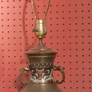 May include: A brass table lamp with a cloisonné vase base. The vase has a colorful floral and geometric design with gold accents. The lamp has a simple, round shade holder.