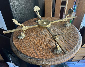 May include: A vintage, round wooden table with a brass decorative top. The brass top features four arms with ornate, stylized bird and floral designs. The table has a dark, aged appearance, suggesting it is an antique or vintage piece.
