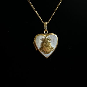 May include: A gold heart-shaped locket necklace with a white mother-of-pearl inlay and a gold crown design.