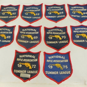 May include: Ten blue and red embroidered patches with the National Rifle Association logo, a gun, and the year and league. The patches are arranged in two rows of five.