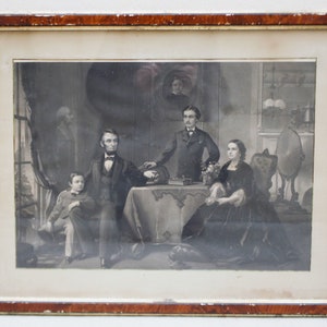 May include: A black and white framed print of a family portrait. The family is posed in a formal setting, with the father seated at a table and the mother and two children standing behind him. The print is in good condition and has a slight yellowing to the paper.