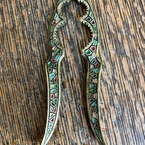 May include: A brass nutcracker with a geometric design in shades of green, red, and blue enamel.