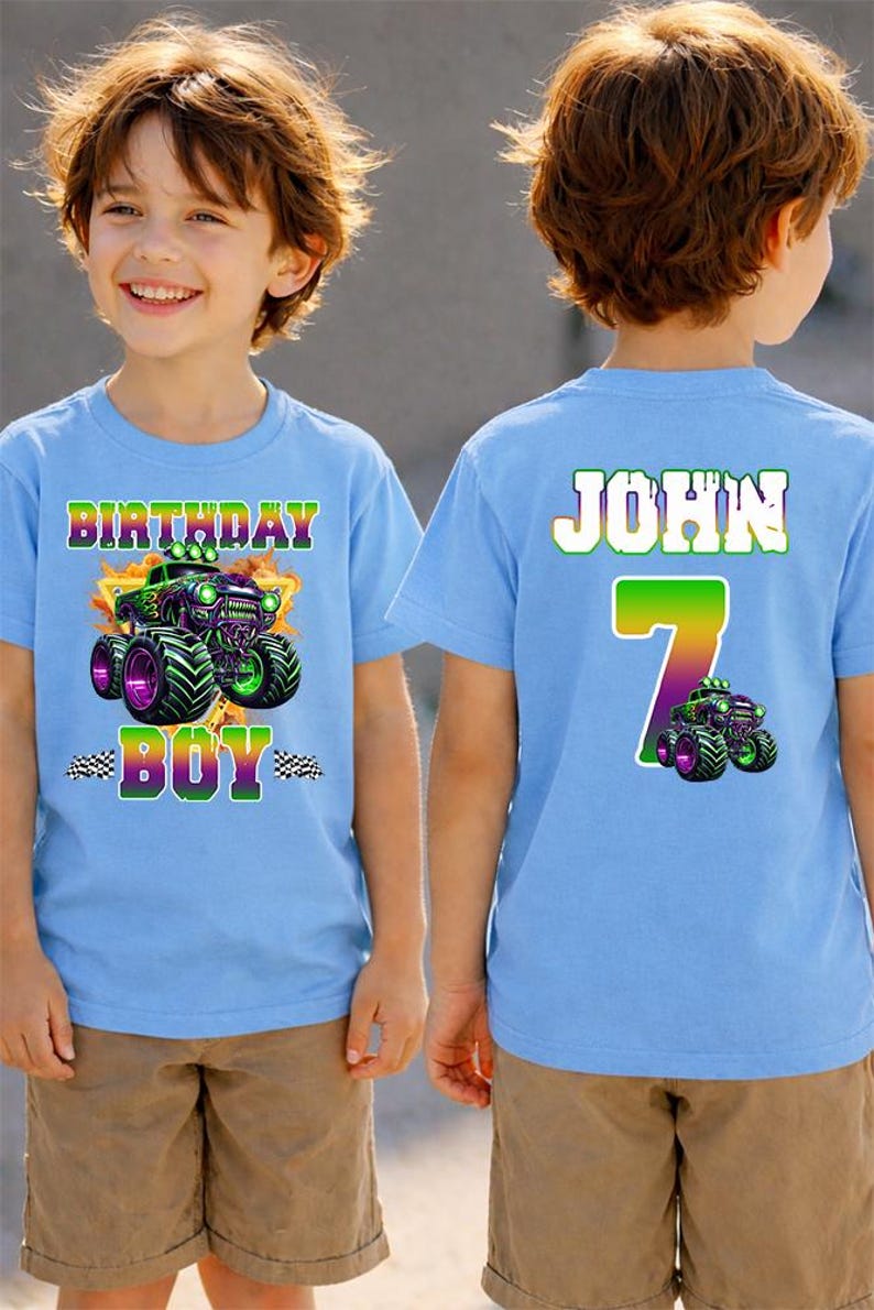 K&ouml;nnte beinhalten: Zwei hellblaue T-Shirts mit einem Monster-Truck-Motiv. Auf einem Shirt steht "BIRTHDAY BOY" und auf dem anderen "JOHN 7". Die Shirts werden von einem jungen Mann getragen, der khakifarbene Shorts tr&auml;gt.