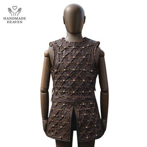 May include: Brown leather vest with intricate studded design, displayed on a mannequin. The vest features a detailed pattern of interwoven straps and small, round studs. The vest is sleeveless and has a split in the back.