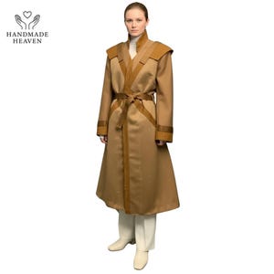 May include: A long, tan coat with brown accents, a matching belt, and a high collar. The coat features decorative trim and is worn with white pants and shoes. The Handmade Heaven logo is in the upper left corner.