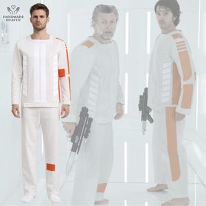 May include: White long-sleeved jumpsuit with orange accents. The jumpsuit features a square neckline, vertical white stripes, and orange patches on the sleeves and knees. The image includes the text "HANDMADE HEAVEN" in a heart-shaped logo.