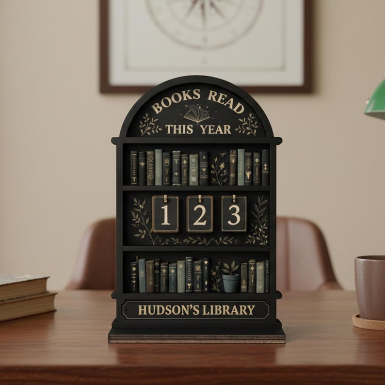 May include: Black wooden bookshelf-shaped calendar with the text "BOOKS READ THIS YEAR" and "HUDSON'S LIBRARY". The calendar displays the numbers 123. The bookshelf is filled with miniature book replicas.