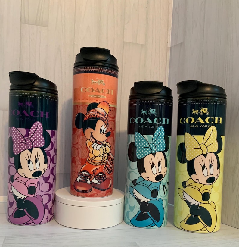 K&ouml;nnte beinhalten: Vier Coach New York Edelstahl-Wasserflaschen mit Disney-Figuren. Jede Flasche hat einen schwarzen Deckel und ein anderes Minnie- oder Mickey Mouse-Design. Die Flaschen sind in den Farbt&ouml;nen Lila, Orange, Blau und Gelb gehalten.