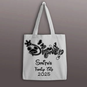 以下が含まれることがあります： 黒いディズニーのロゴとテキストが入った白いトートバッグ。バッグには、ミッキーマウス、コック帽、蝶のディズニーロゴが描かれています。ロゴの下には「Smith's Family Trip 2025」と書かれています。