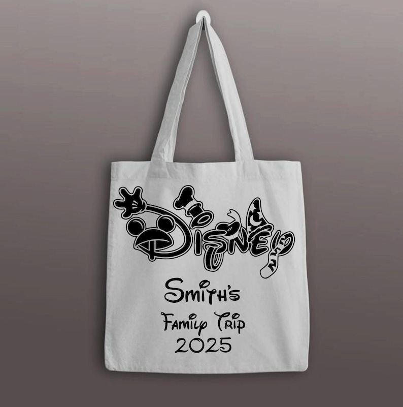 以下が含まれることがあります： 黒いディズニーのロゴとテキストが入った白いトートバッグ。バッグには、ミッキーマウス、コック帽、蝶のディズニーロゴが描かれています。ロゴの下には「Smith's Family Trip 2025」と書かれています。