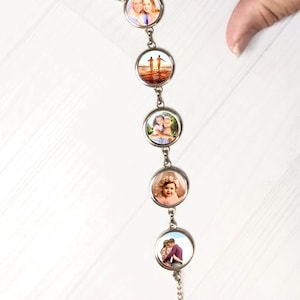May include: A silver-toned bracelet featuring five circular charms, each displaying a different photograph. The photos include images of people, couples, and children. The bracelet is connected by small links and a chain.