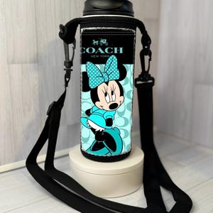 K&ouml;nnte beinhalten: Eine schwarze und t&uuml;rkisfarbene Wasserflasche mit einem Minnie Mouse-Design und dem Coach New York-Logo. Die Flasche hat einen schwarzen Deckel und einen schwarzen Trageriemen. Die Minnie Mouse-Grafik ist in T&uuml;rkis und Schwarz gehalten.