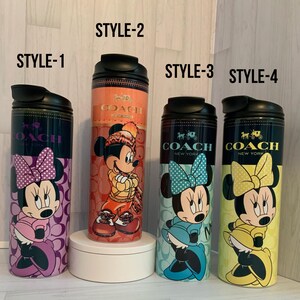 K&ouml;nnte beinhalten: Vier isolierte Coach New York-Becher mit Disney-Figuren. Stil 1 zeigt Minnie Mouse mit einer lila Schleife, Stil 2 Mickey Mouse in Winterkleidung, Stil 3 Minnie mit einer blauen Schleife und Stil 4 Minnie mit einer gelben Schleife.