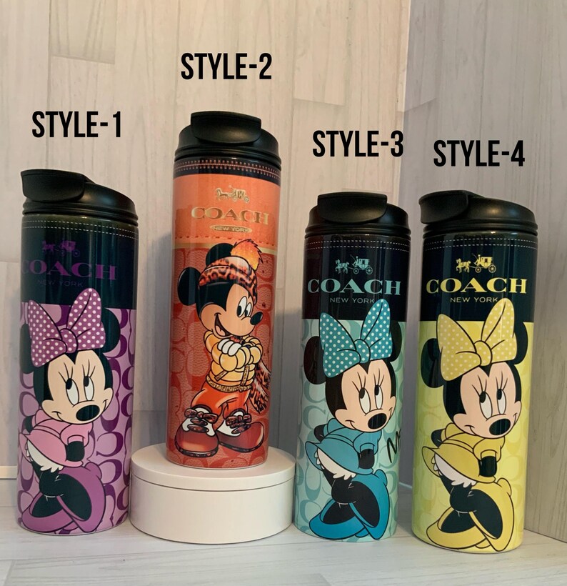 K&ouml;nnte beinhalten: Vier isolierte Coach New York-Becher mit Disney-Figuren. Stil 1 zeigt Minnie Mouse mit einer lila Schleife, Stil 2 Mickey Mouse in Winterkleidung, Stil 3 Minnie mit einer blauen Schleife und Stil 4 Minnie mit einer gelben Schleife.