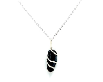 May include: A black gemstone pendant necklace. The dark, irregular-shaped stone is wrapped in silver-colored wire and hangs from a delicate silver chain. The necklace is set against a white background.