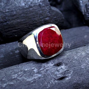 May include: A silver ring featuring a large, square-cut ruby gemstone. The ruby is a deep red hue, set in a polished silver band. The text "CraftFineJewelry" is visible on the ring.